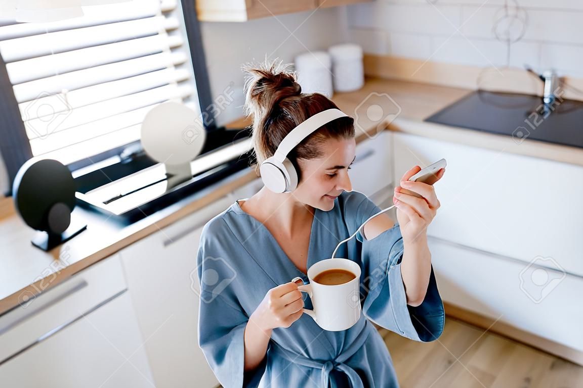 Mujer joven escuchando música y disfrutando de una taza de café por la mañana, en su cocina.