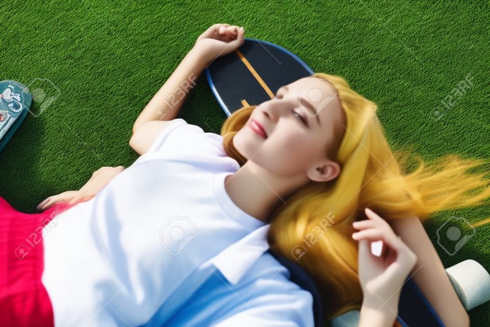 High angle view of young woman lying on the grass with her skateboard.