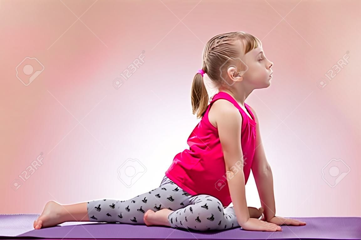 Kleines Mädchen sitzen in der Yogahaltung auf farbigem Hintergrund.
