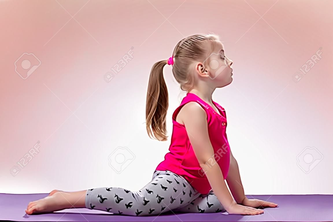 Kleines Mädchen sitzen in der Yogahaltung auf farbigem Hintergrund.