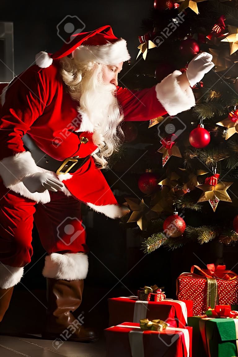 산타가 어두운 방에 크리스마스 트리 아래 선물을 쥐고