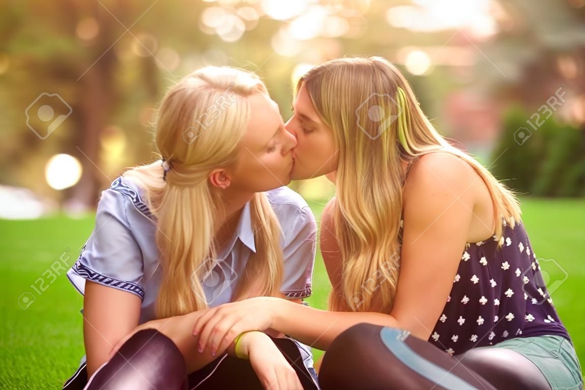Woman and teen daughter giving kiss to each other while cuddling on green summer lawn in park