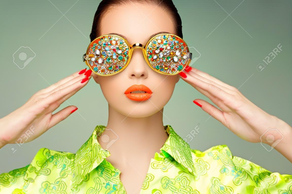 Portret pięknej młodej kobiety z kolorowych okularów. Moda Uroda. Idealny makijaż. Kolorowe dekoracje. Biżuteria