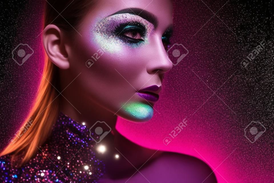 Ritratto di bella donna con le scintille sul suo viso. La ragazza con arte compone di luce di colore. Moda modello colorato con il make-up. Bianco e nero