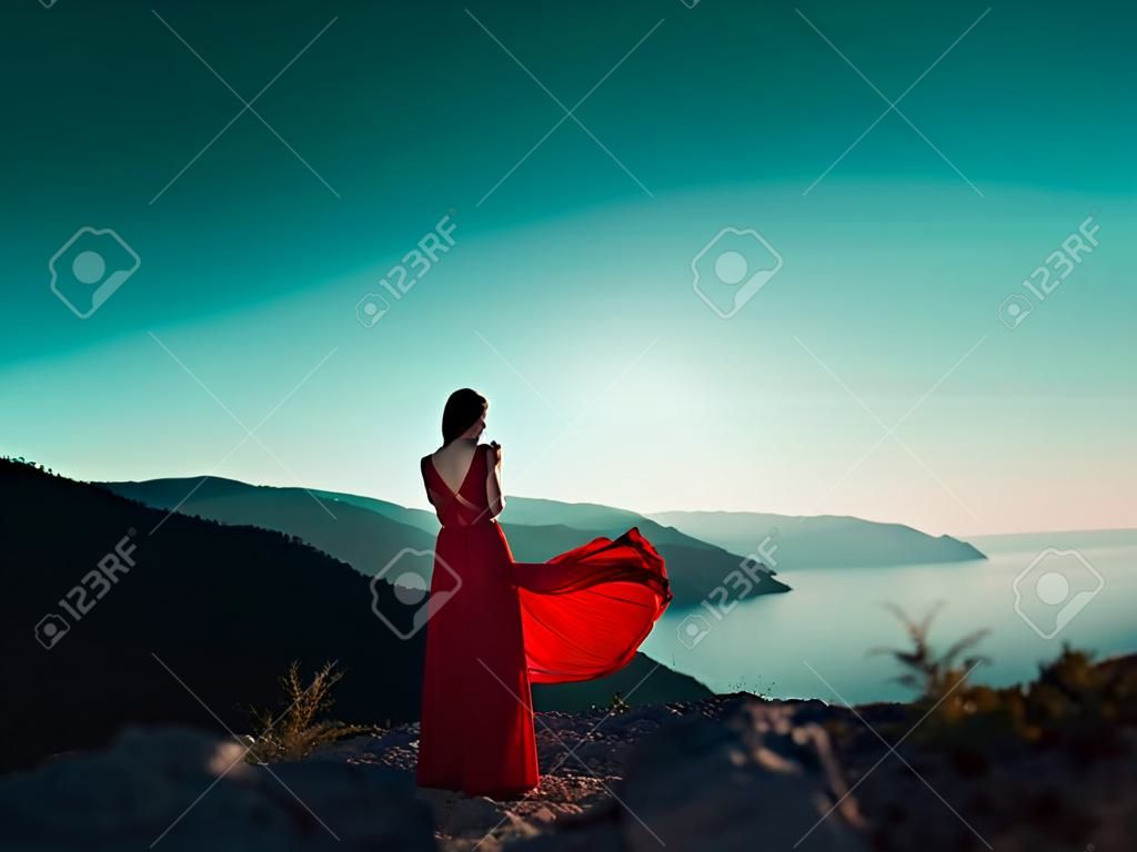 Jeune femme belle en robe rouge regardant les montagnes mer. Fille de la nature sur fond de ciel bleu. photo de mode