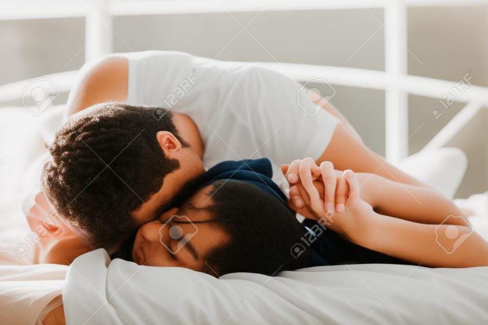 jóvenes amantes que se besan en la cama centran en la mano
