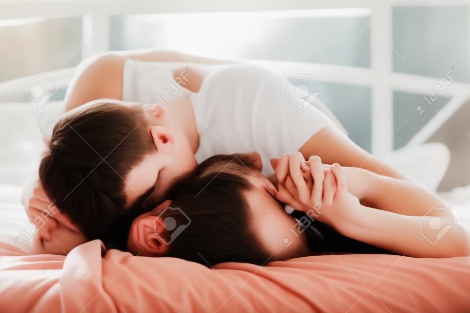 jóvenes amantes que se besan en la cama centran en la mano