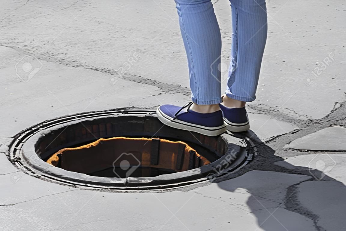 The girl steps into the open sewer hatch, sewer hatch without lid