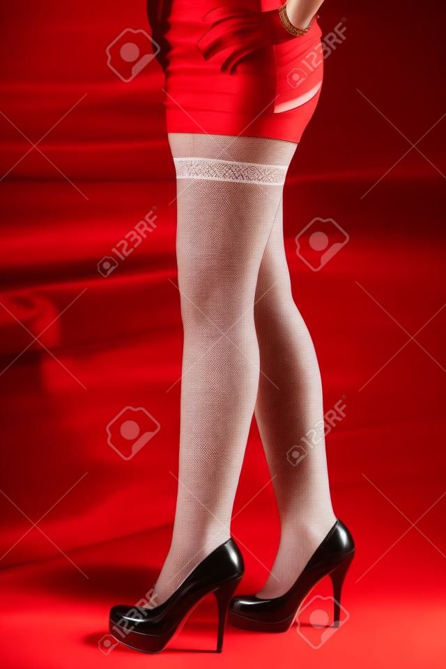 Red High Heels - Frau mit Minirock da stehen mit ihren langen Beinen und weißen Nylons