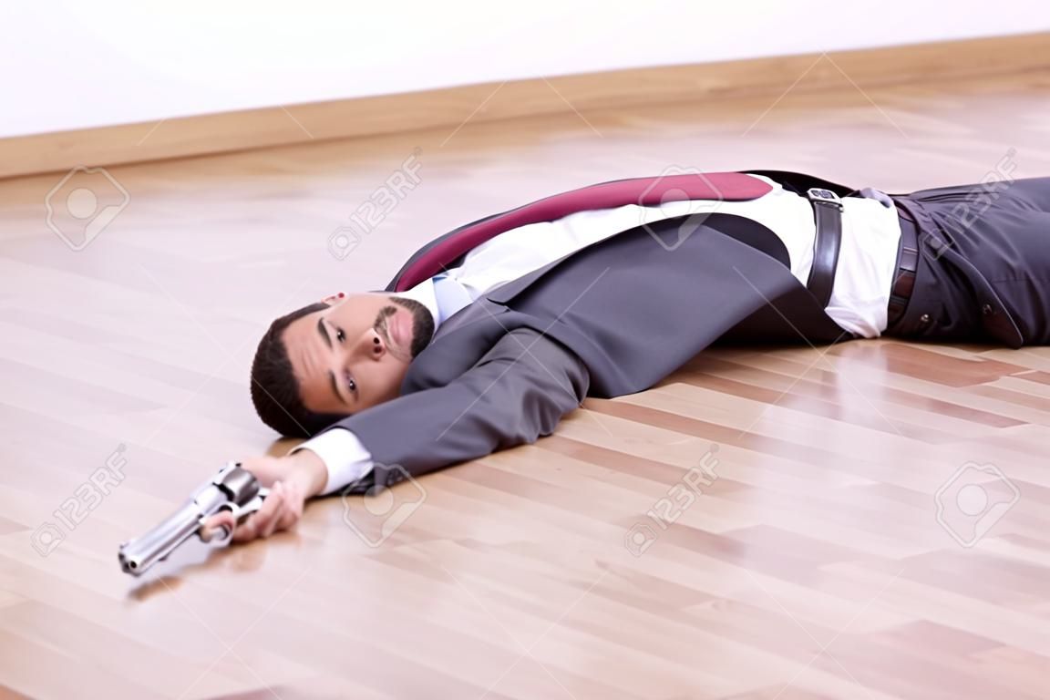 Businessman lying dead in the office floor with a gun in his hand