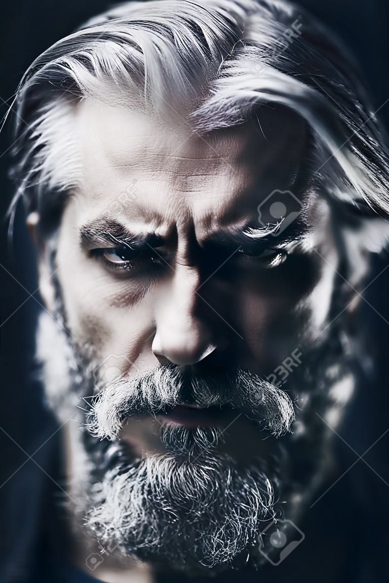 Artistic portrait of angry mid aged man with white hair and beard. Shallow depth of field