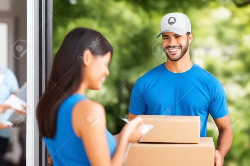 Mujer de aceptar una entrega de dos cajas de cartón con una orden o un regalo de firmar el portapapeles digital para el repartidor sonrisa amistosa en la puerta