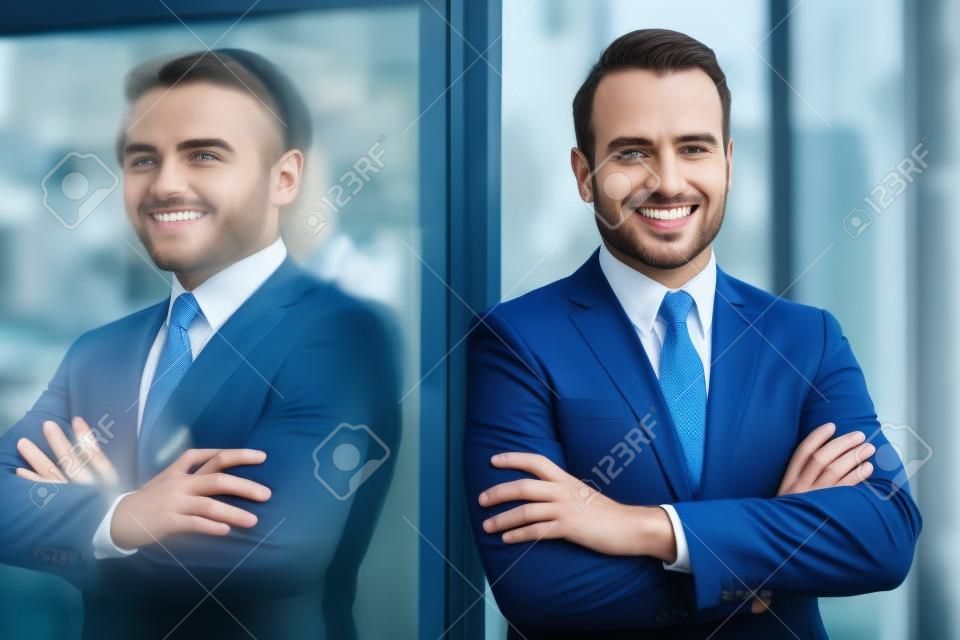 Single confident and handsome male businessman in blue suit and necktie with grin leaning on window outdoors