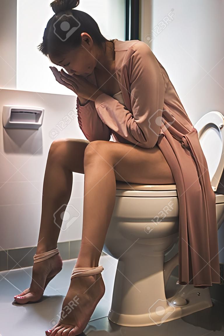 vrouw zittend op toilet kom met stress gebaar, gezondheid concept