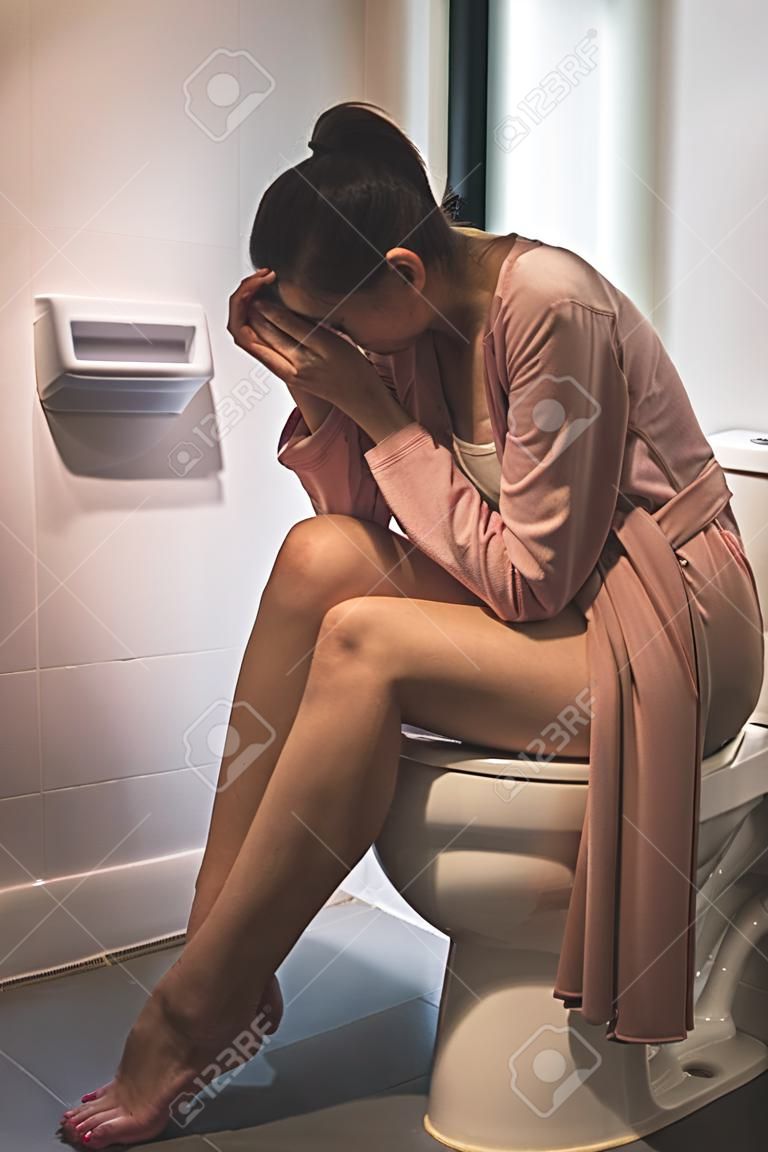 vrouw zittend op toilet kom met stress gebaar, gezondheid concept