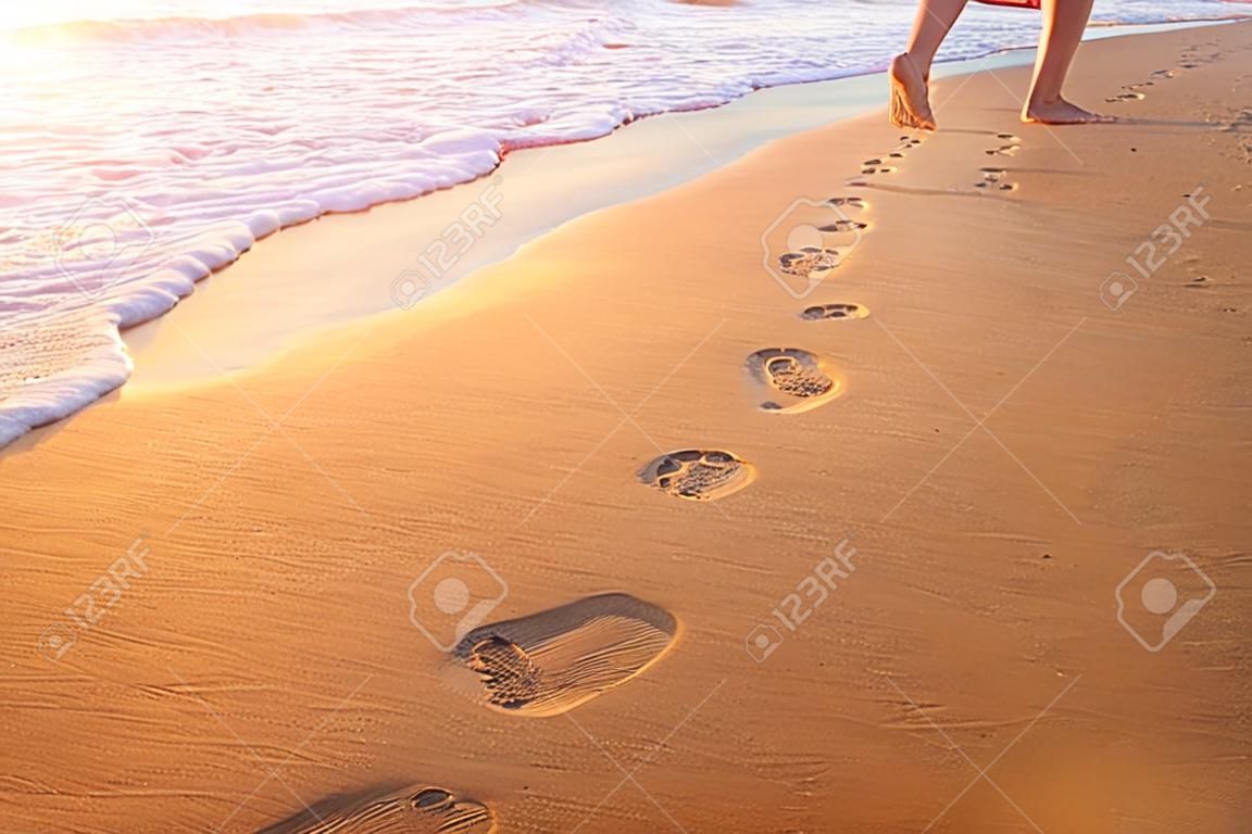 plaża, fala i ślady stóp o zachodzie słońca