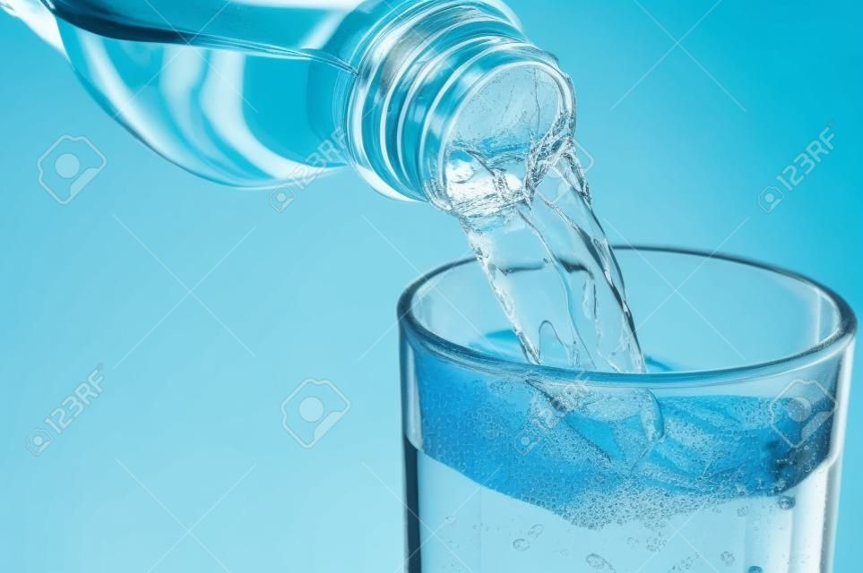 Gießen von Wasser aus Flasche in Glas auf blauem Hintergrund