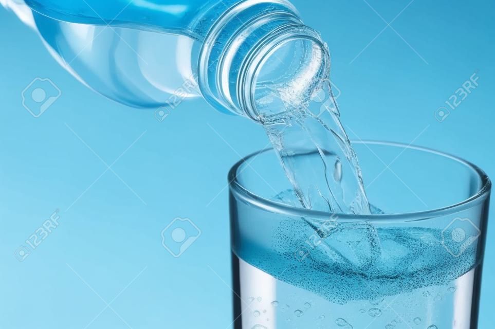 Gießen von Wasser aus Flasche in Glas auf blauem Hintergrund