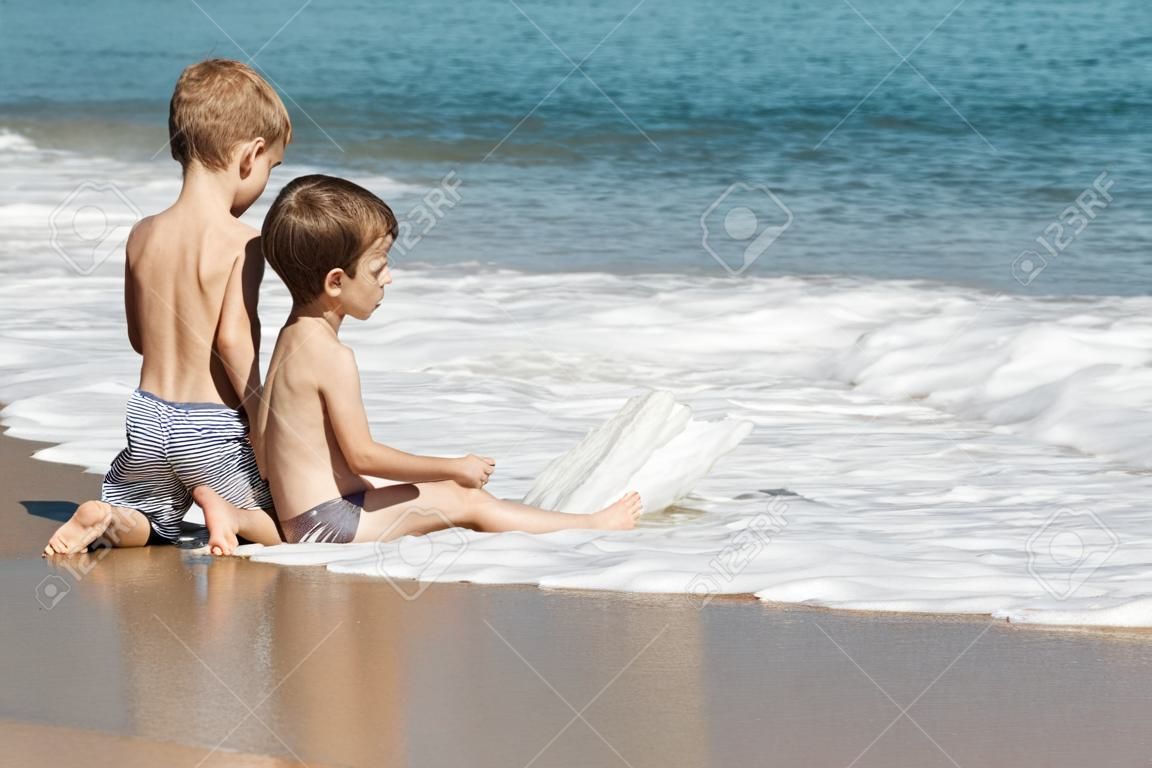 Summer vacations - two little child boy brothers playing on blue sea sand beach