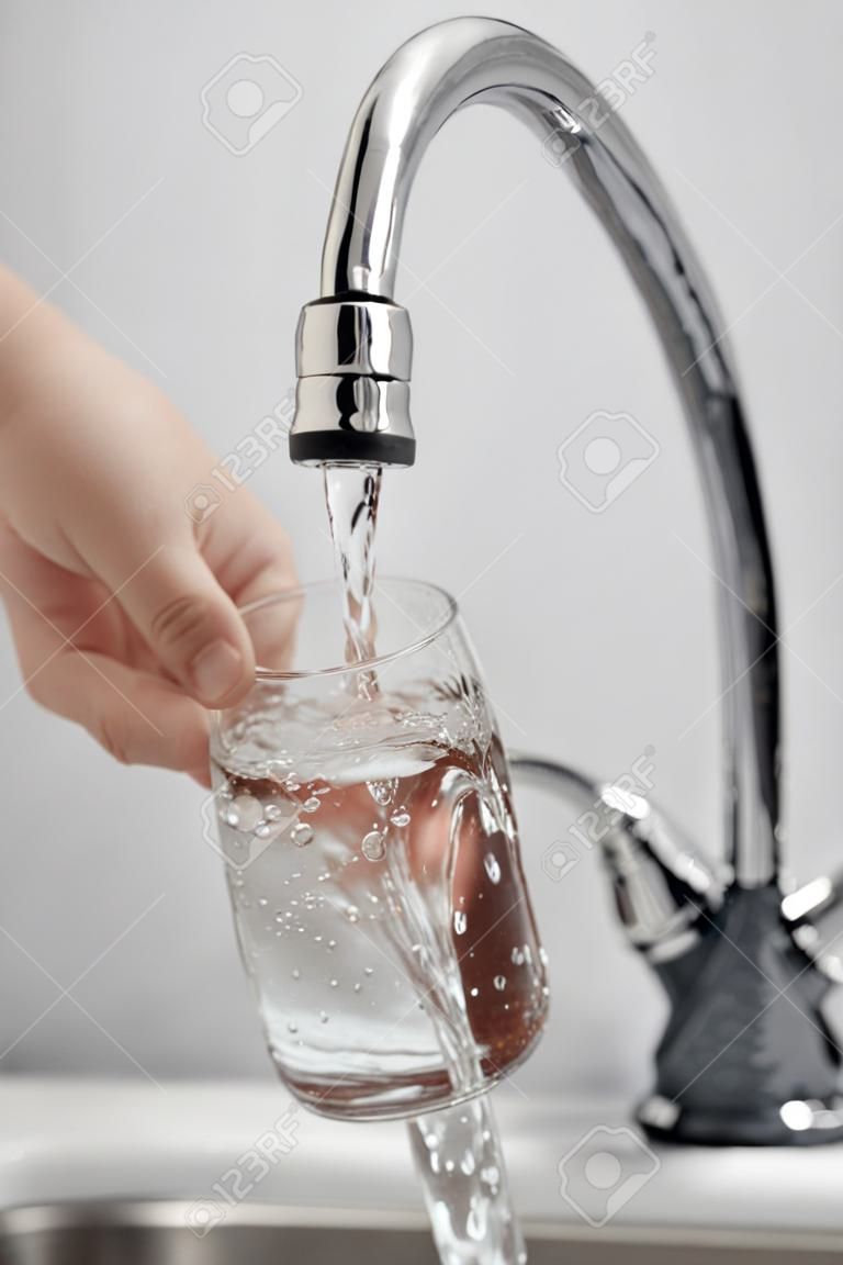 La mano del hombre de vidrio de verter el agua bebida fresca en el grifo de la cocina