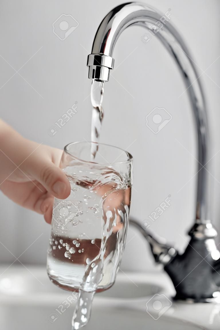 Человека стеклом держит руку заливки свежей воды напиток в кухонный кран