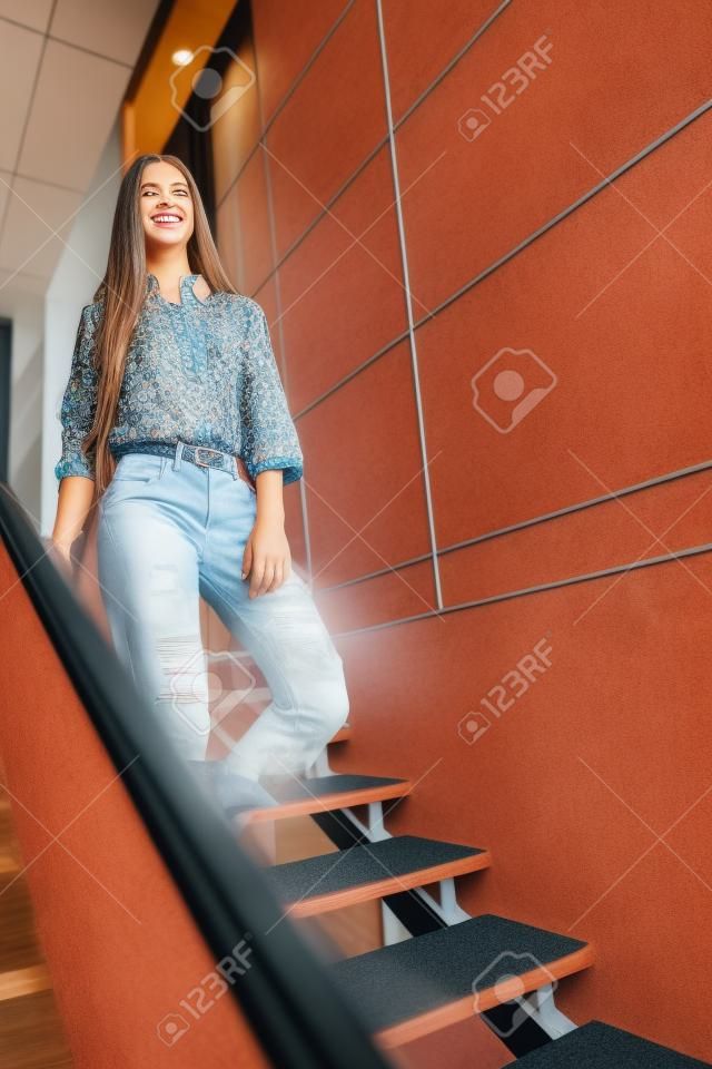 La chica alegre está esperando a alguien. Ella está de pie en la escalera y sonriendo