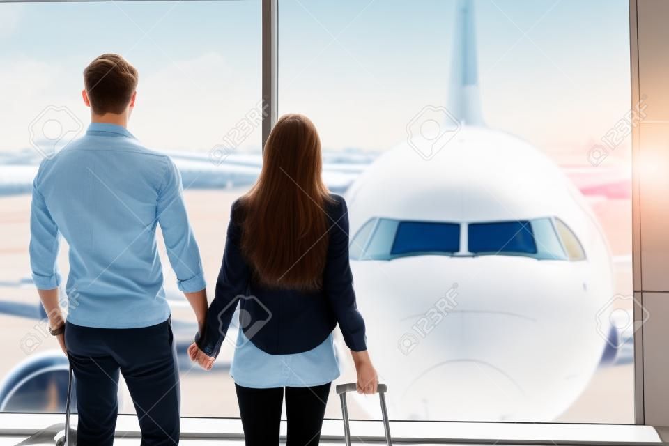 Forward to future. Young loving couple is watching plane though window before departure. They are standing at airport and holding hands