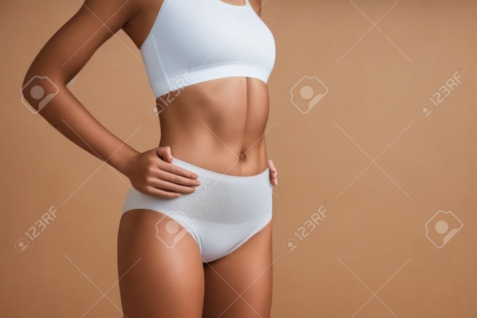 Close Up Of Fit Female Body Wearing Tight Panties And Bra. She Is Holding  Hands On Waistline. Copy Space On Right Side. Isolated On Background  Фотография, картинки, изображения и сток-фотография без роялти.