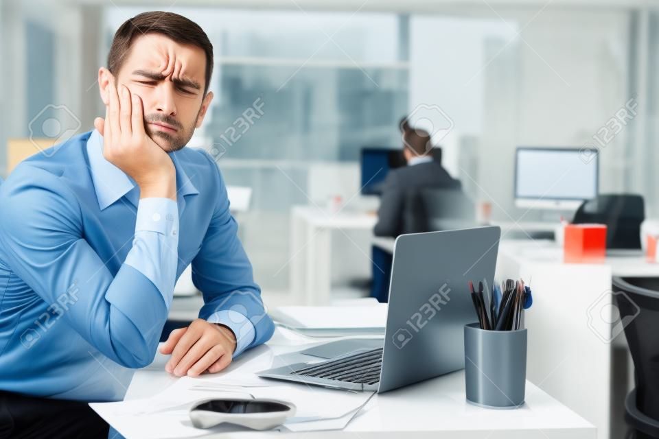 オフィスでラップトップで作業している間、歯の痛みを感じる失望したビジネスマンの肖像画。労働概念における疾患