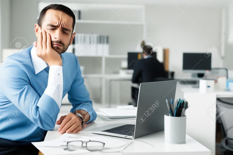 オフィスでラップトップで作業している間、歯の痛みを感じる失望したビジネスマンの肖像画。労働概念における疾患