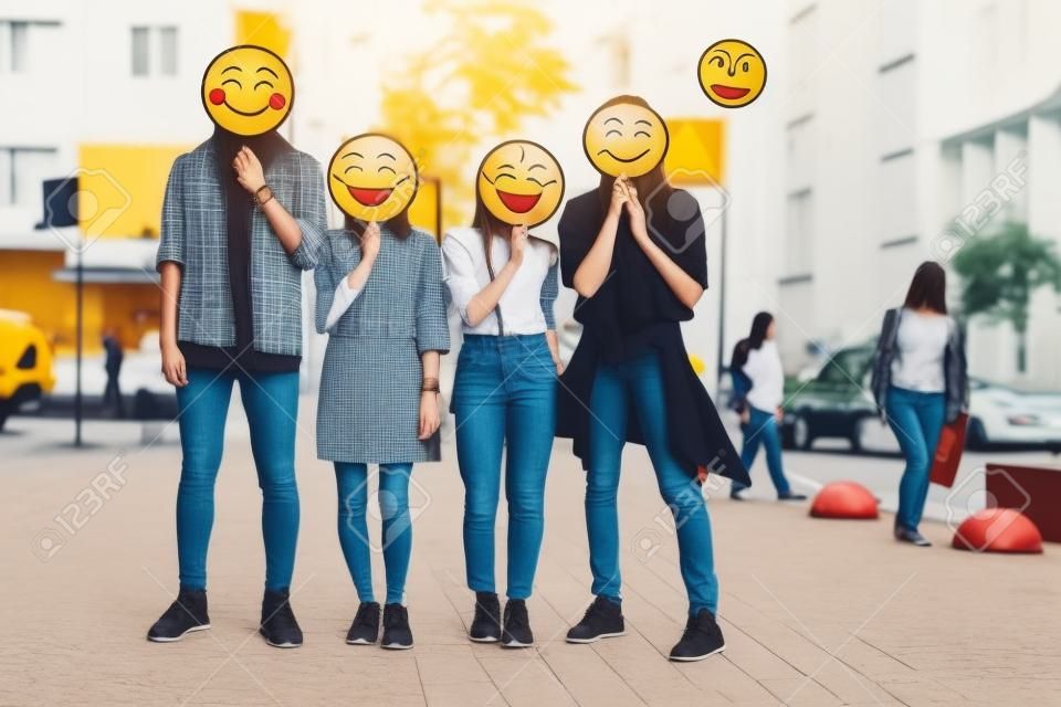 Volledige lengte portret van positieve meisjes en mannen met emoji gezichten staan op straat