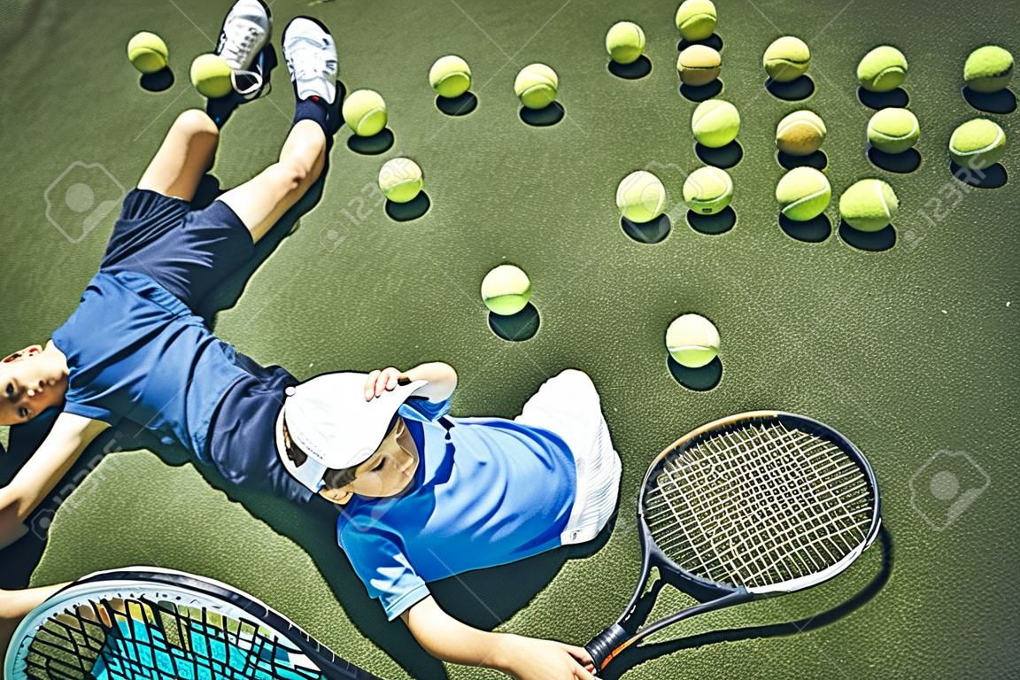 Top view full length calm boy relaxing on court while keeping racket