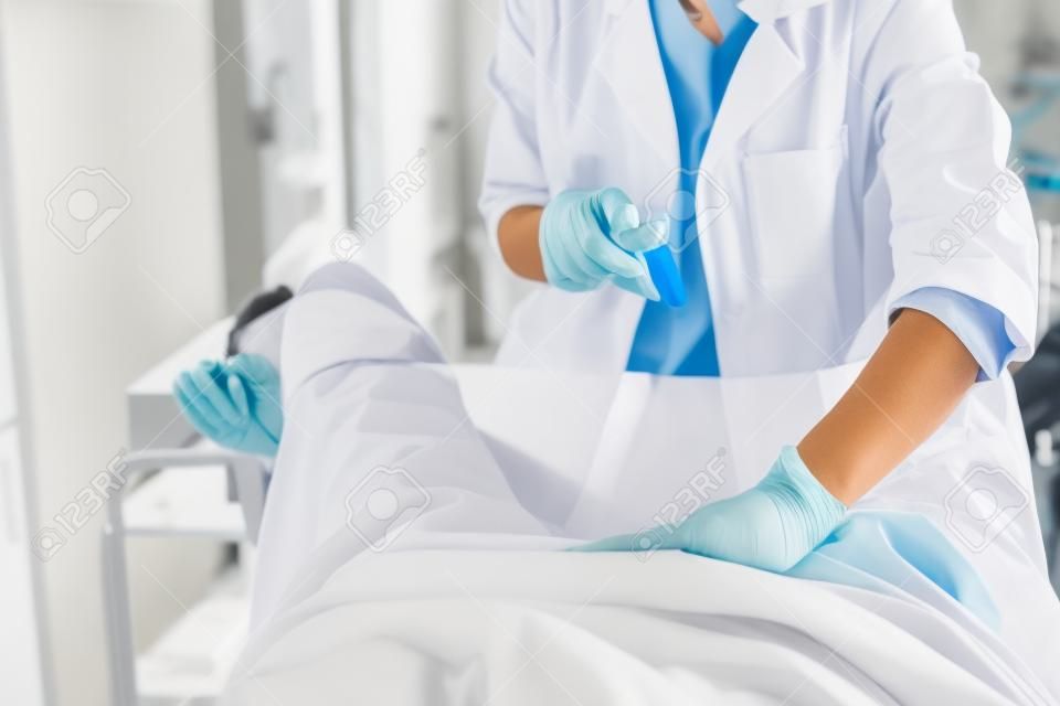 Bijgesneden portret van gynaecoloog in witte labjas en steriele handschoenen met behulp van vaginaal speculum tijdens bekkenonderzoek