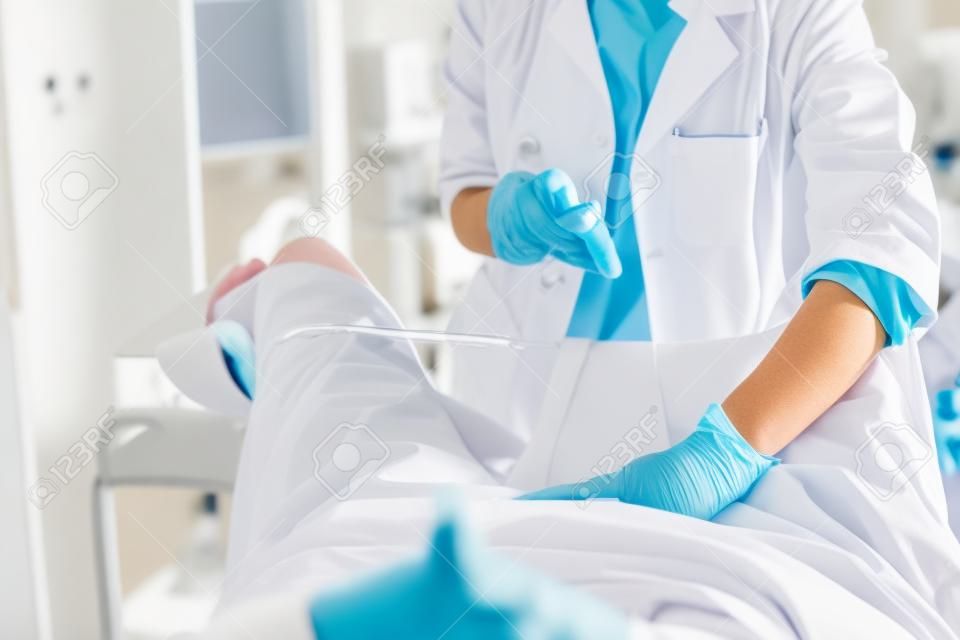 Retrato recortado del ginecólogo en bata blanca de laboratorio y guantes estériles con espéculo vaginal durante el examen pélvico