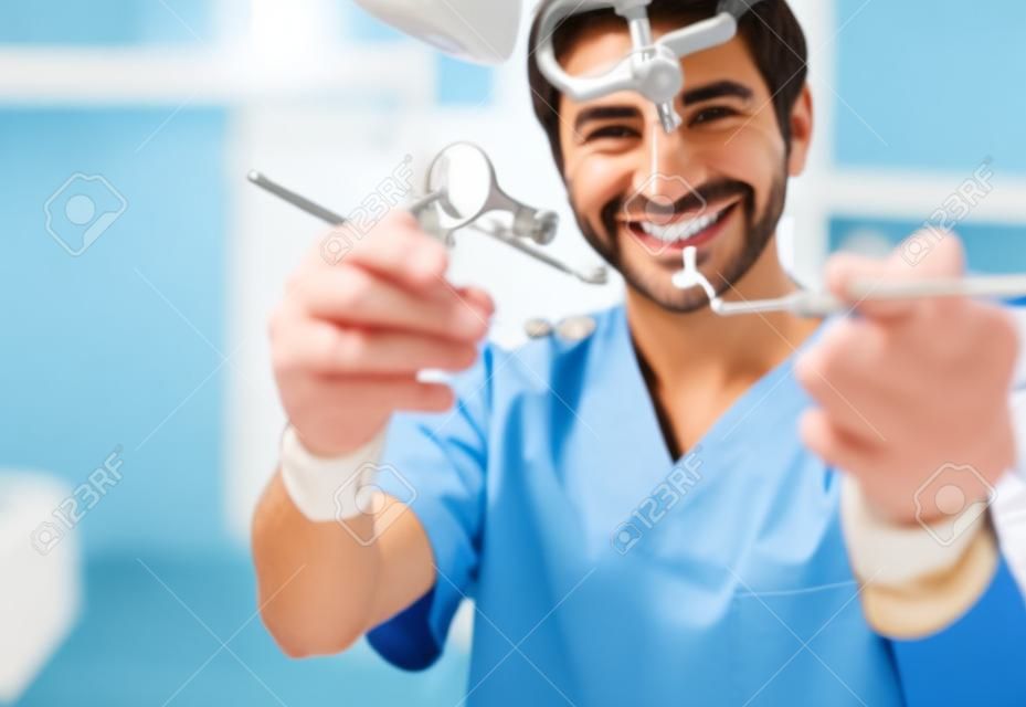 Dentista maschio allegro che dimostra gli strumenti su sfondo sfocato