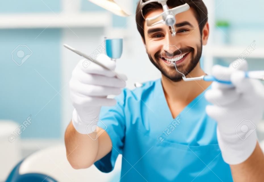 Dentista maschio allegro che dimostra gli strumenti su sfondo sfocato