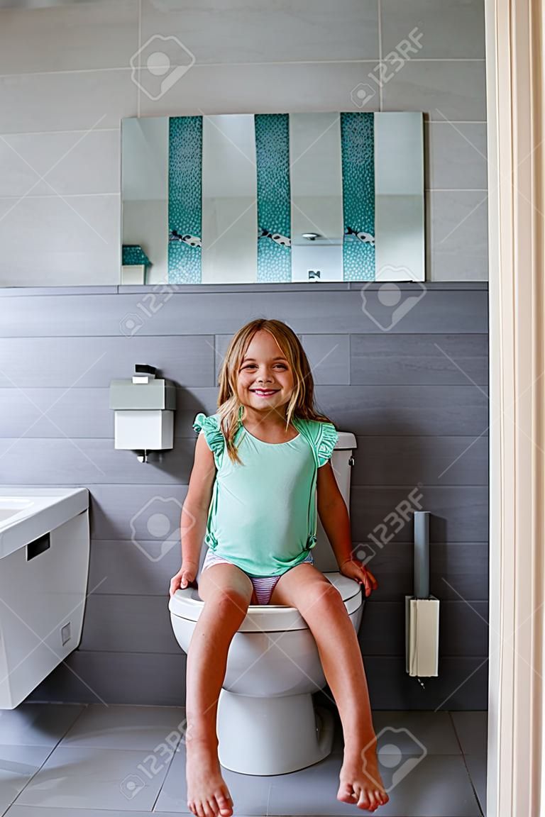Smiling girl sitting on a toilet in bathroom