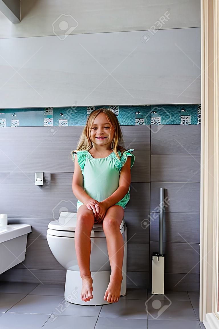 Smiling girl sitting on a toilet in bathroom