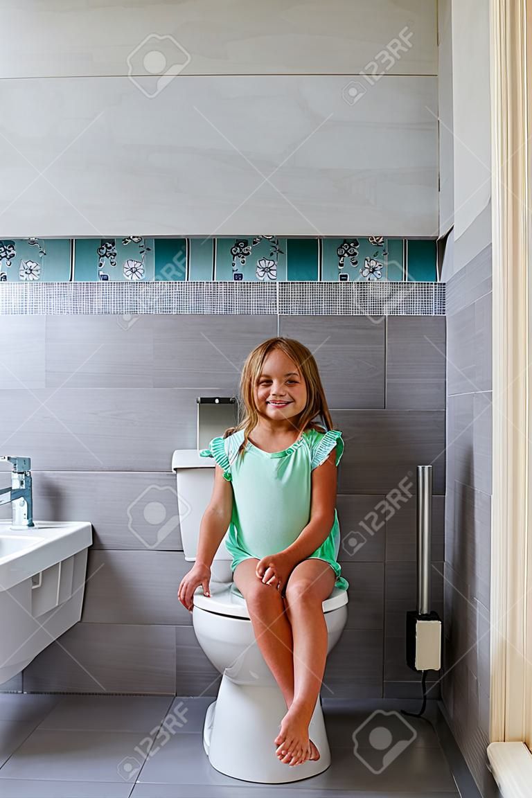 Lächelndes Mädchen, das auf einer Toilette im Badezimmer sitzt