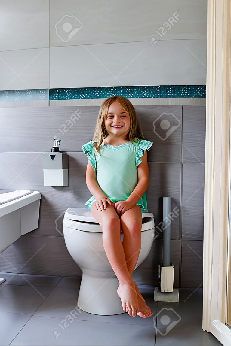 Lächelndes Mädchen, das auf einer Toilette im Badezimmer sitzt