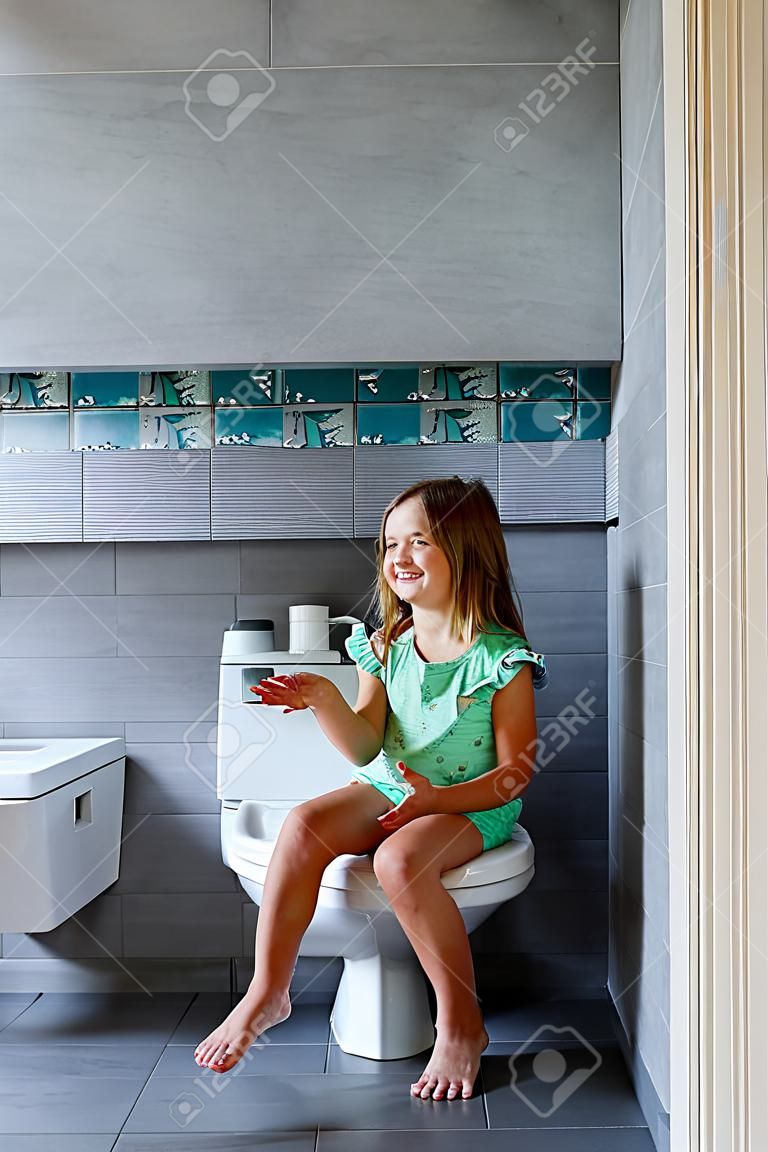 Heureuse jolie fille assise sur les toilettes à la maison