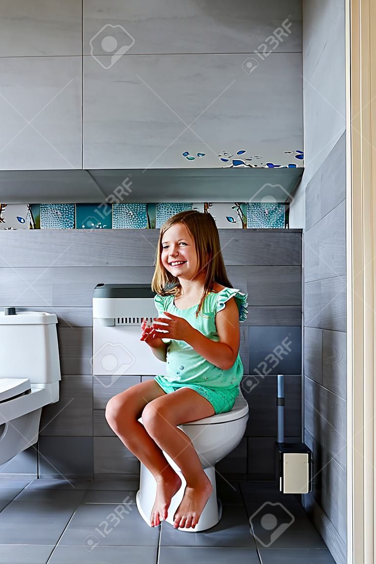 Happy cute girl sitting on the toilet at home