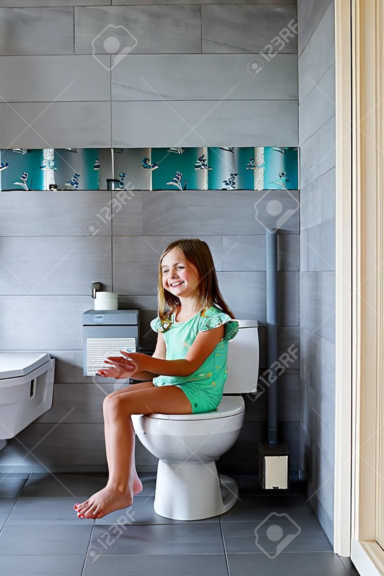 Glückliches süßes Mädchen, das zu Hause auf der Toilette sitzt