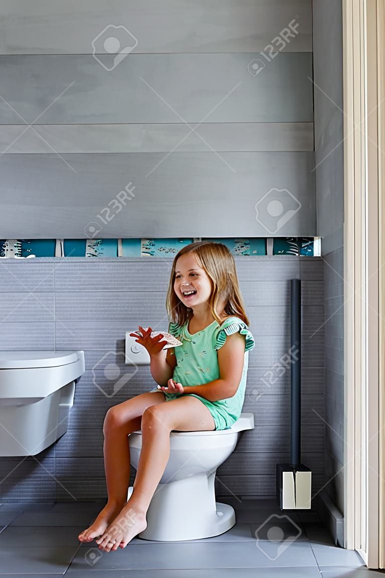 Happy cute girl sitting on the toilet at home