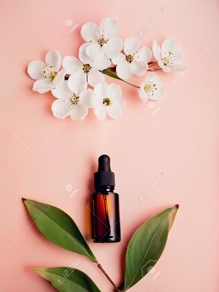 Glass bottles with oil, perfume on a pink background with blooming cherry. Flat lay, minimalism. Cosmetical tools.