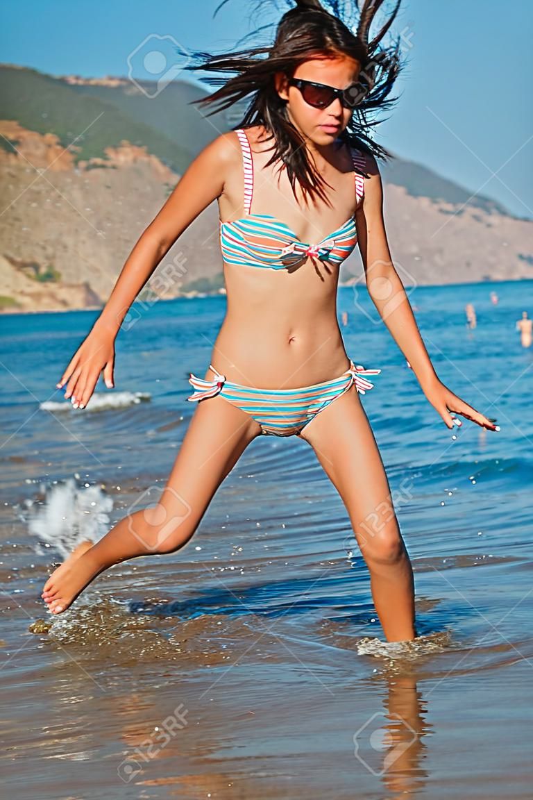 Muchacha adolescente joven que juega con las olas en la playa