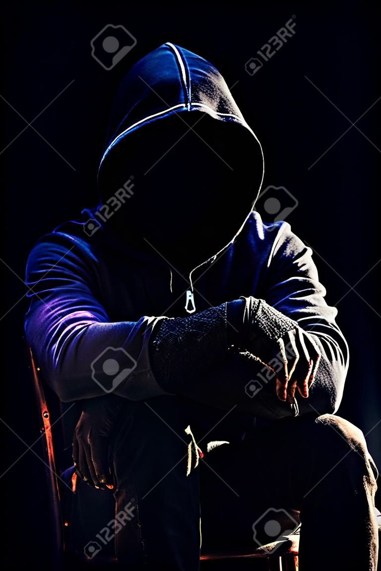Photo d'un homme harceleur étranger d'horreur effrayant en capuche noire et vêtements assis sur une chaise sur fond sombre.