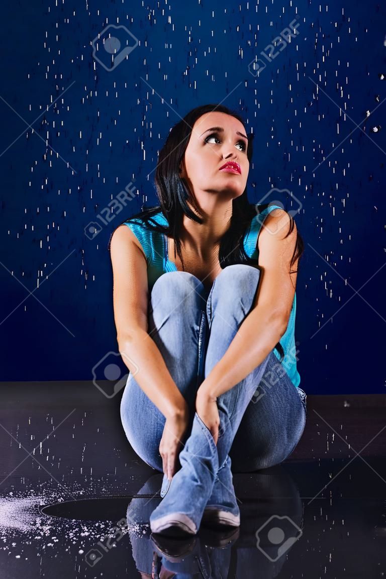 La muchacha manchada se sienta en la lluvia y mira hacia arriba