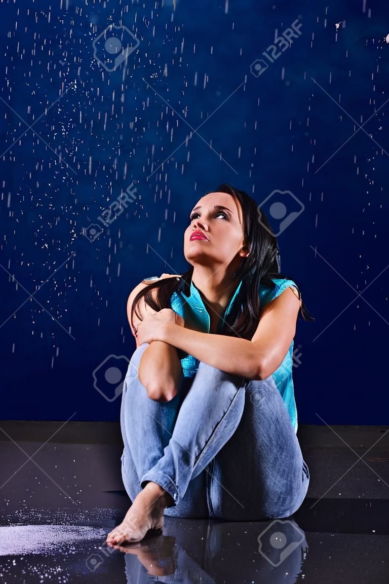 La muchacha manchada se sienta en la lluvia y mira hacia arriba