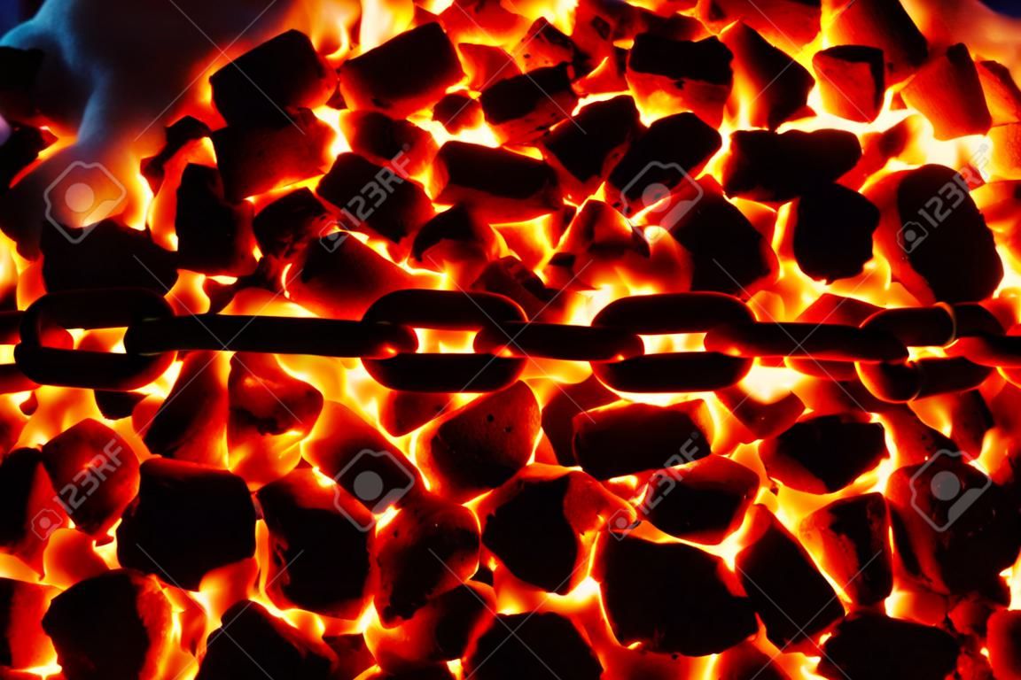 Os elos de uma corrente vermelha-quente deitada em um antracite de carvão em chamas.